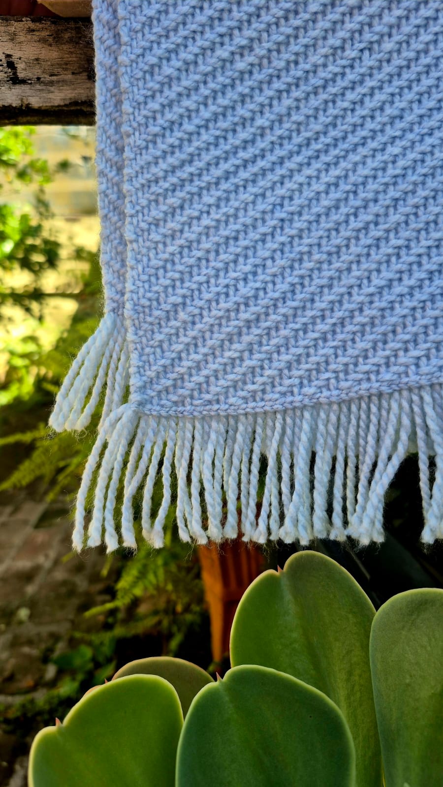 manta para bebé tejida en telar de color celeste con trama diagonal. detalle lateral y flecos